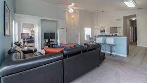 A modern living room with a sectional sofa, a dining area with bar stools, and a kitchen in the background. - West Haven IHR 4079 (Davenport)