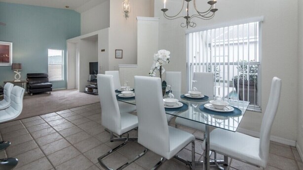 A dining area with a glass table, white chairs, and a chandelier. - West Haven IHR 4079 (Davenport)