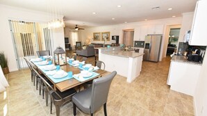A spacious kitchen with modern appliances, a dining area with a long table set for six, and a living area with a sofa and TV. - Watersong Resort - 6 bed - Private Pool - IHR 3103 (Davenport)