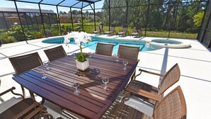 An outdoor patio with a wooden table and wicker chairs, overlooking a swimming pool. - Watersong Resort - 6 bed - Private Pool - IHR 3103 (Davenport)