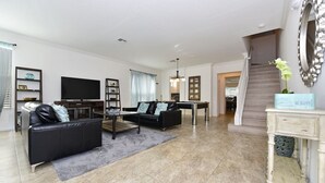 A modern living room with a black leather sofa, a flat-screen TV, and a staircase leading to another level. - Watersong Resort - 6 bed - Private Pool - IHR 3103 (Davenport)