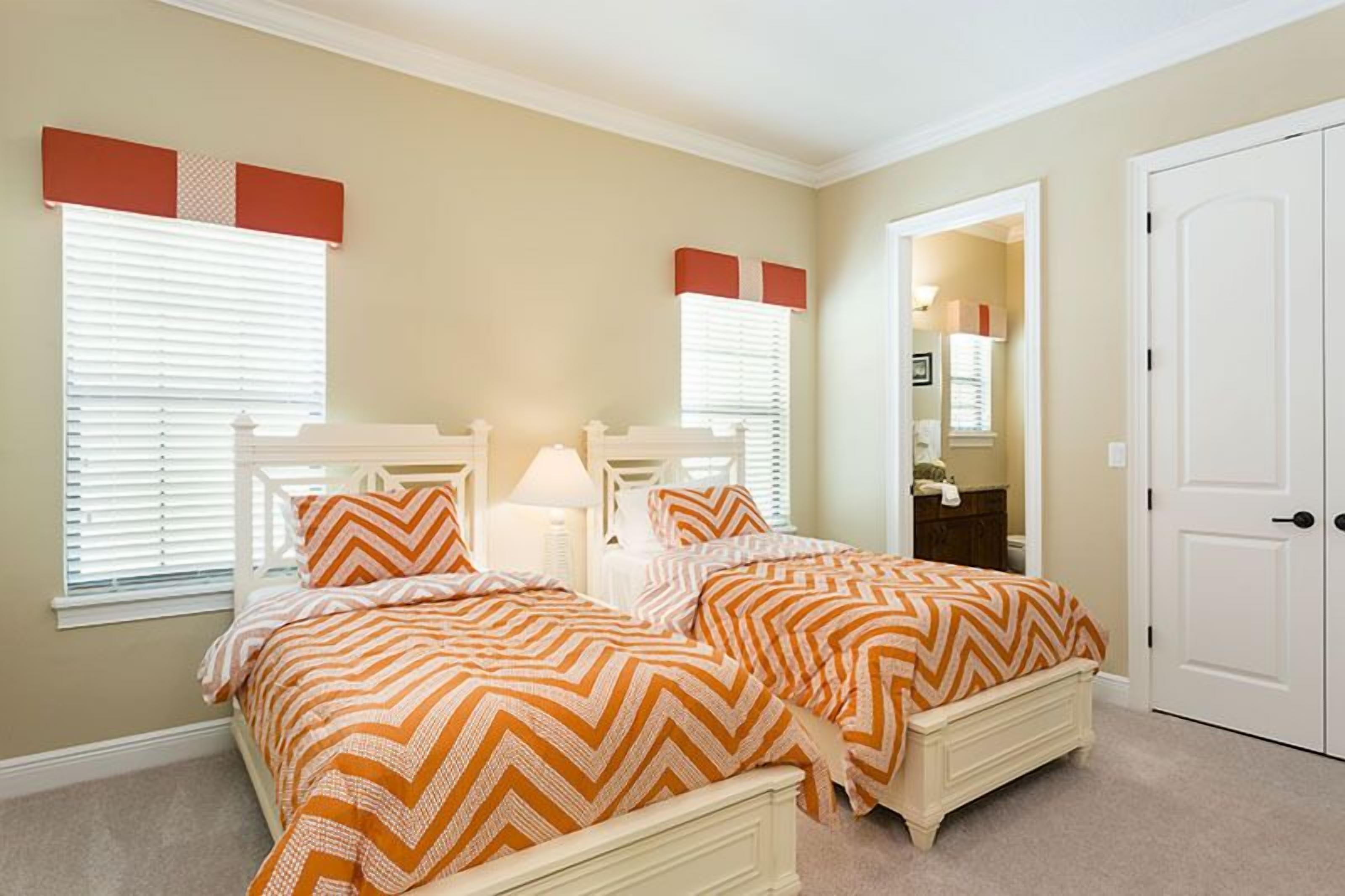 A bedroom with two beds, white headboards, and orange and white striped bedding.
