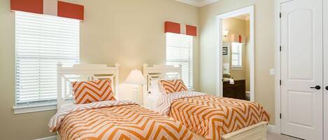 A bedroom with two beds, white headboards, and orange and white striped bedding.
