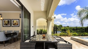 An outdoor patio with a glass-top table, wicker chairs, and a pool. - 5 Bed 5 Ba Villa with Game Room, Pool & Spa (Kissimmee)