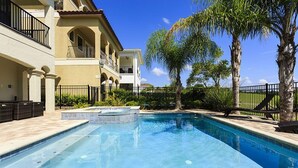 A swimming pool with a clear blue water, surrounded by a fence, and a building with balconies in the background. - 5 Bed 5 Ba Villa with Game Room, Pool & Spa (Kissimmee)