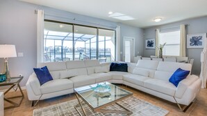A modern living room with a sectional sofa, a glass coffee table, and large windows offering a view of the city. - 5 Bed 5 Ba Home W Pool & Spa (Kissimmee)