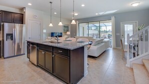 A modern kitchen with a central island, stainless steel appliances, pendant lighting, and a view to the living area. - 5 Bed 5 Ba Home W Pool & Spa (Kissimmee)