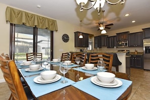 Enjoy meals in this dining area with a long table, dark cabinetry, and a ceiling fan.