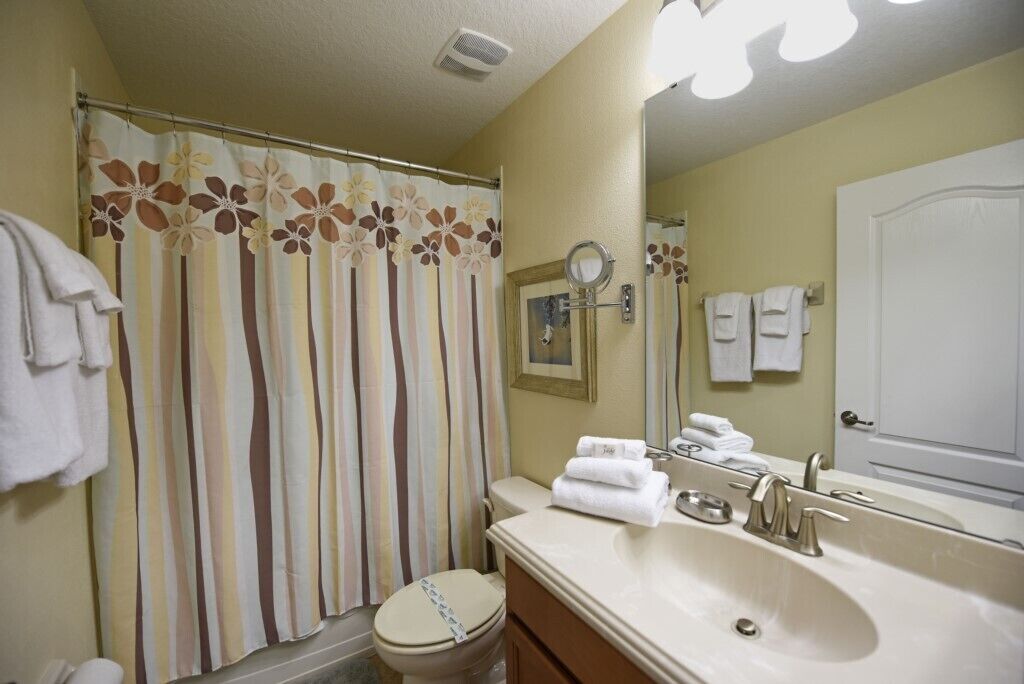 A bathroom with a shower curtain, toilet, sink, and mirror.