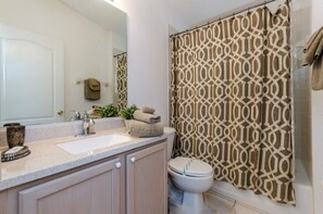 Un baño con un lavamanos blanco, un inodoro y una cortina de ducha estampada.