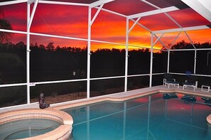 Una piscina interior con vistas a la puesta de sol a través de amplios ventanales, un jacuzzi y varias sillas de descanso.