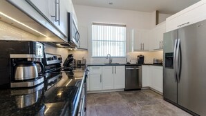 A modern kitchen with stainless steel appliances, white cabinetry, and a large window providing natural light. - 1802nhd (Davenport)