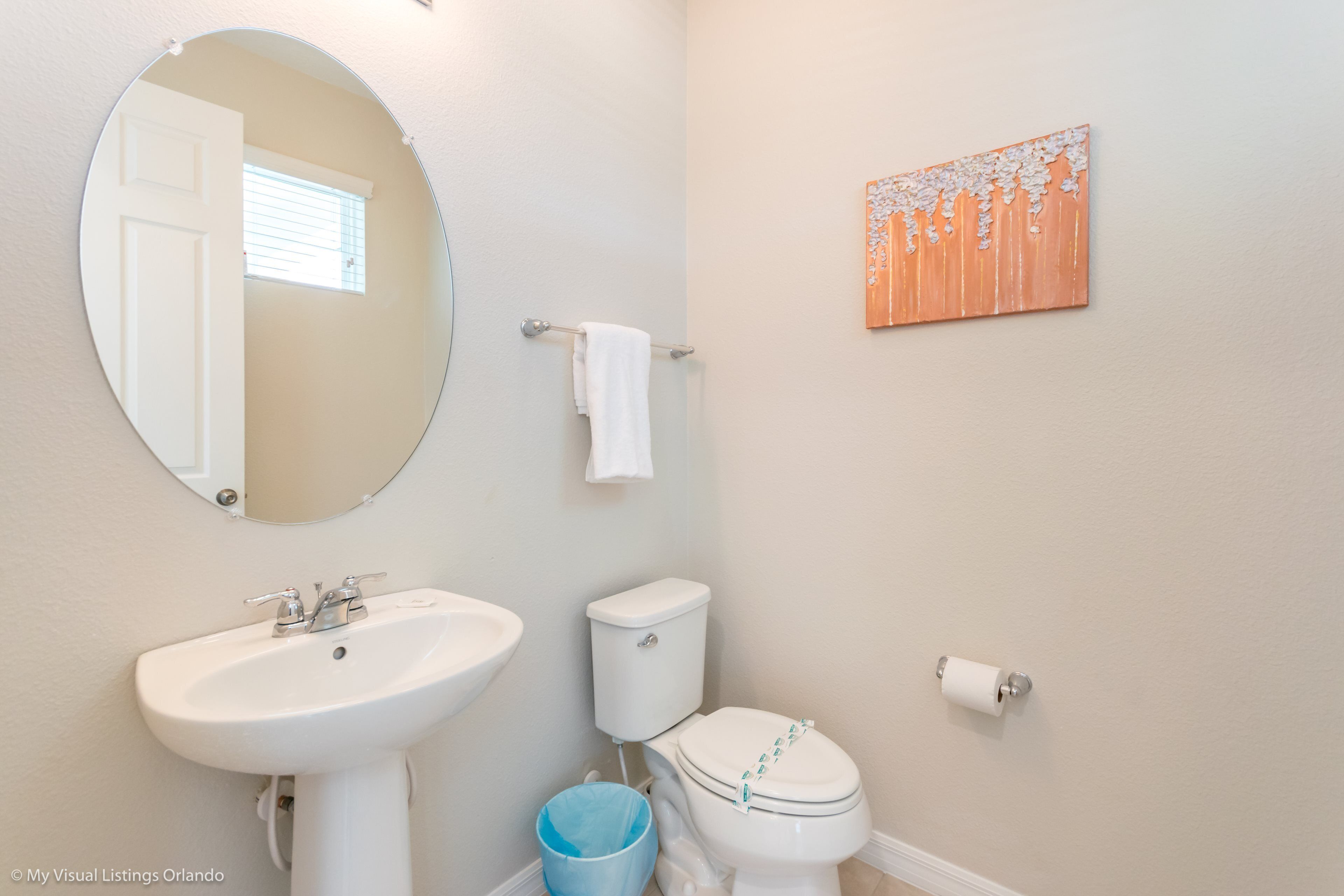 A bathroom with a white sink, toilet, and a blue trash bin.