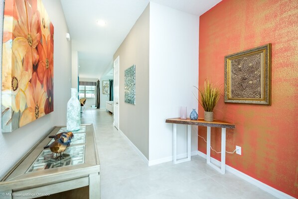 A hallway with a glass display case containing decorative birds, a large floral painting, and a textured wall art piece.