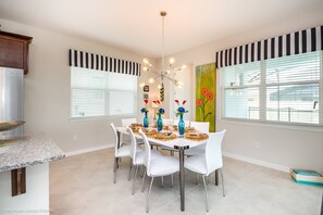 A dining area with a white table set for six, surrounded by white chairs.