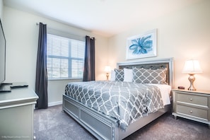 A bedroom with a bed, bedside tables, a nightstand, a dresser, a window with curtains, and a wall art piece. - Champions Gate 6 Bedroom 5 BH (Davenport)