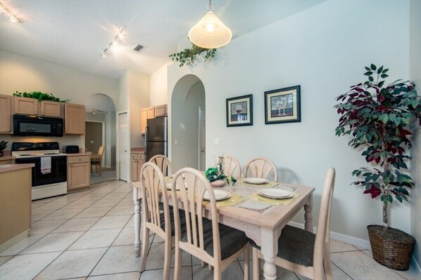 A modern kitchen with wooden cabinets, a dining table set for four, and a large potted plant.