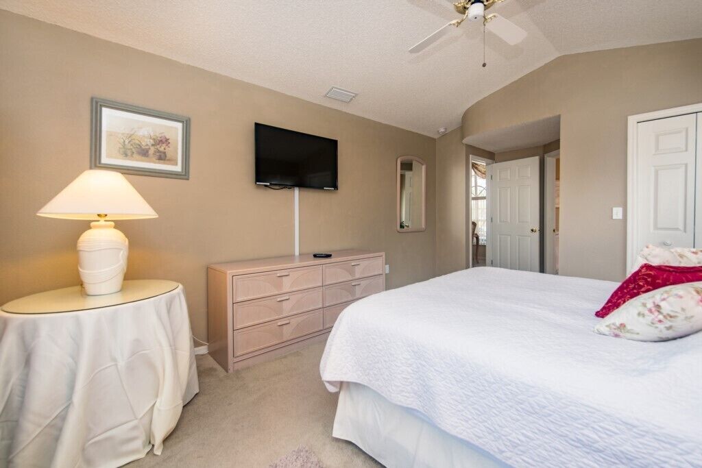 A bedroom with a bed, a dresser, a TV, a lamp, and a door.