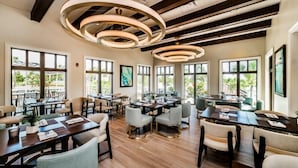 Un vaste espace dédié à la salle à manger, avec de nombreuses tables et chaises, de grandes fenêtres offrant une vue sur la verdure et un design moderne au niveau du plafond.