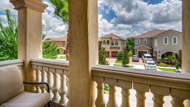A residential area with a balcony, columns, and a view of houses with a clear sky. - Elegant 5 BD, 5 BH Villa (Kissimmee)