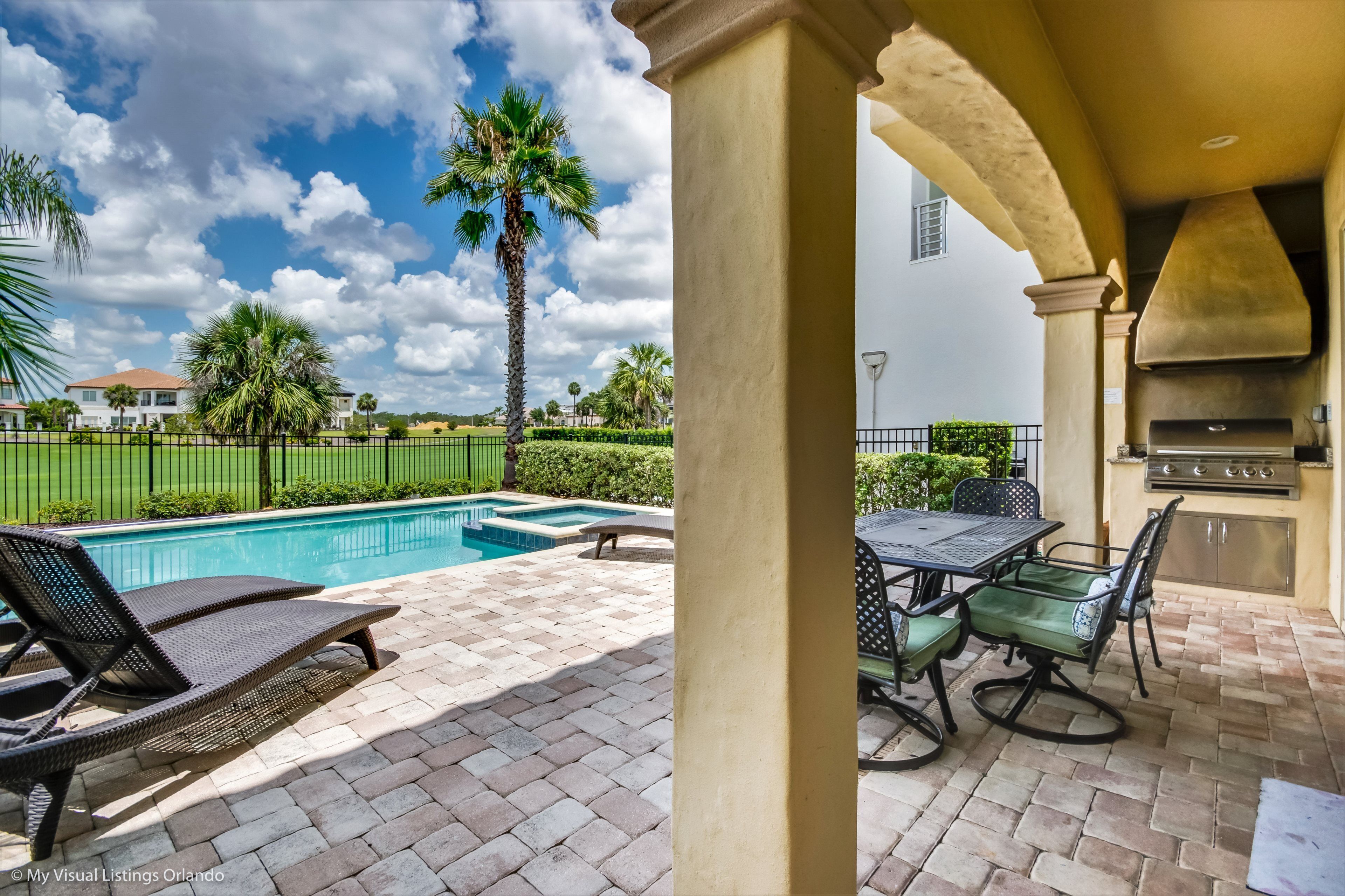 A poolside area with lounge chairs, a barbecue grill, and a view of a residential neighborhood.