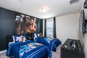 Quarto com duas camas, um pôster grande de personagens de Star Wars, uma televisão e uma mesinha de centro com um controle remoto.