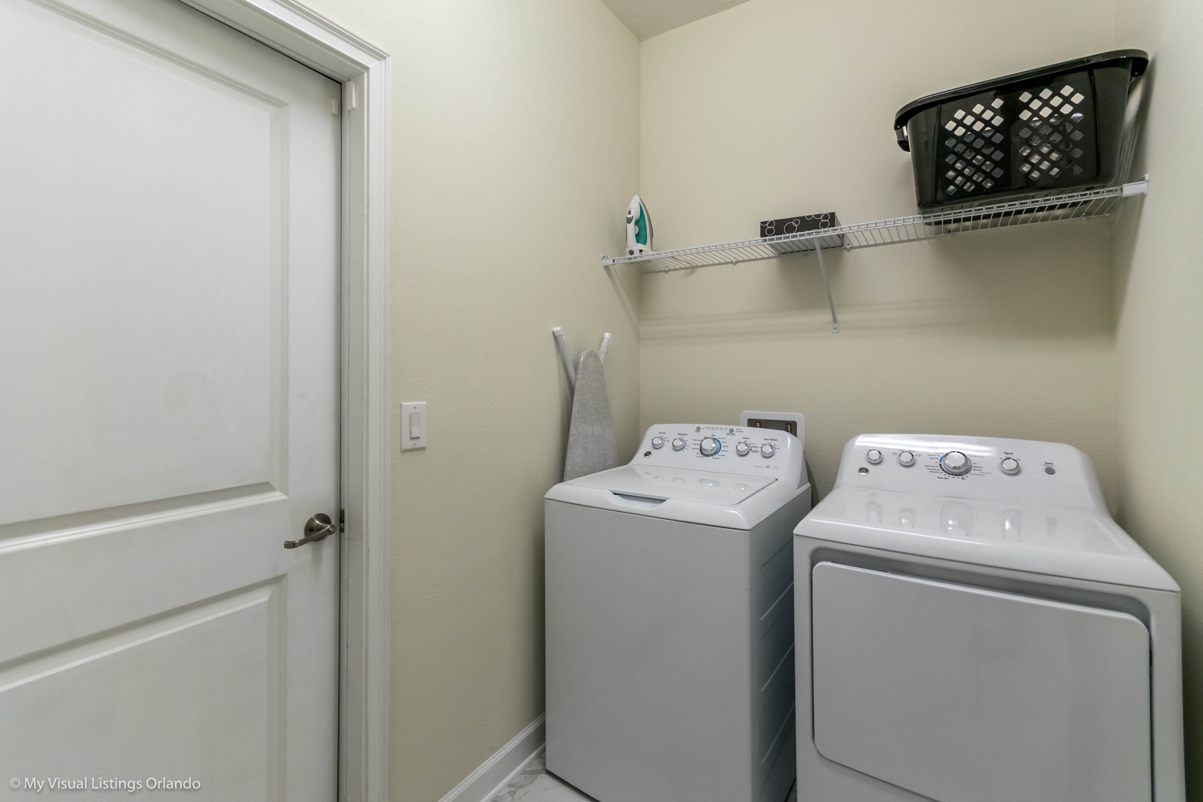 A laundry area with two white washing machines, a white door, and a shelf with a black basket.