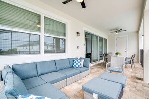 A covered patio area with a blue sofa, a dining table with chairs, and a ceiling fan.