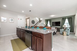 A modern kitchen with granite countertops, a dishwasher, and a dining area with a sofa and TV. - Amazing 6 Bedroom 5 Bathroom Solara Resort Villa (Kissimmee)