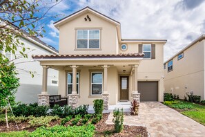 A two-story house with a front porch, stone pillars, and a garage. - Amazing 6 Bedroom 5 Bathroom Solara Resort Villa (Kissimmee)