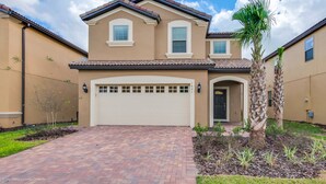 A two-story house with a beige exterior, a garage, and a well-maintained front yard with a palm tree. - 1631la Luxury 6 Bed Villa With Pool & Spa (Kissimmee)