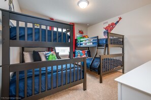 A room with three bunk beds, each with blue bedding and pillows, and a Spider-Man wall decal.