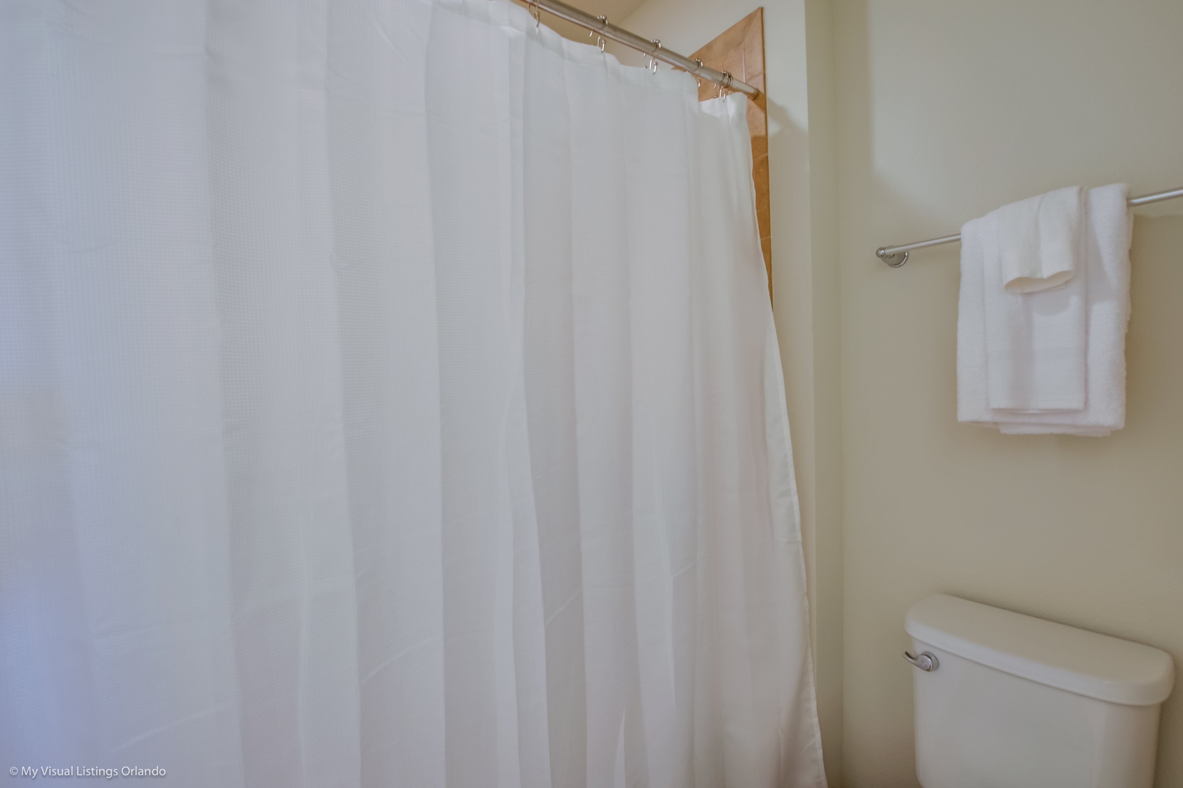 A bathroom with a white shower curtain, a toilet, and a towel rack with two towels.