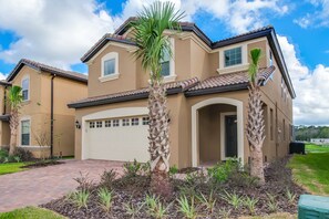 A two-story house with a beige exterior, a garage, and palm trees in the front yard. - 1631la Luxury 6 Bed Villa With Pool & Spa (Kissimmee)
