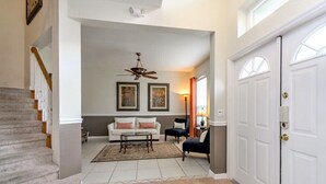 A spacious living room with a white sofa, a coffee table, and a ceiling fan. A staircase leads to another level, and a door is visible on the right. - 337 Belfry (Davenport)