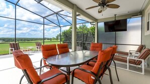 A covered patio with a round table and orange chairs, a ceiling fan, and a TV mounted on the wall. - 337 Belfry (Davenport)