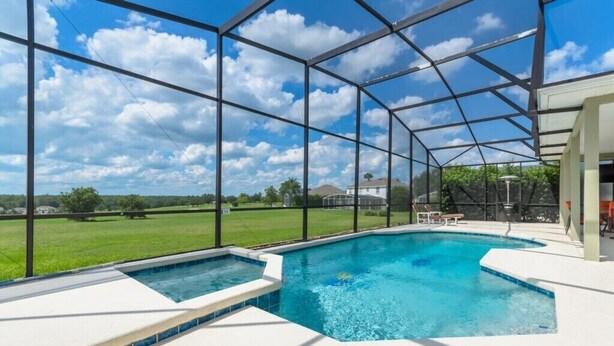 A swimming pool with a glass enclosure, surrounded by a white deck, and a view of a green landscape. - 337 Belfry (Davenport)