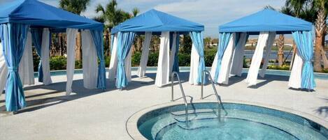 A pool area with three blue and white canopies, a central pool, and palm trees in the background.