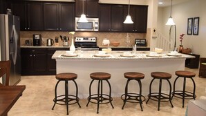 A modern kitchen with dark cabinets, a large island with stools, a microwave, and a coffee maker. - Windsor at Westside IHR 3100 (Kissimmee)