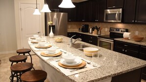 A modern kitchen with dark cabinets, stainless steel appliances, and a granite countertop. - Windsor at Westside IHR 3100 (Kissimmee)
