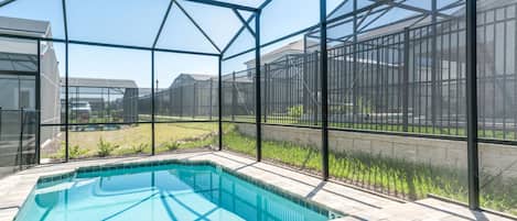 Una piscina con cerramiento de vidrio, rodeada por una valla metálica, y vistas a una zona residencial.