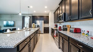 Una cocina moderna con gabinetes de madera oscura, encimeras de granito, electrodomésticos de acero inoxidable y un televisor de pantalla plana.