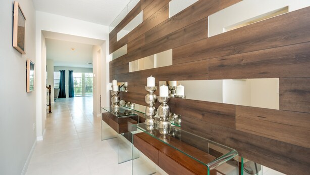Un pasillo moderno con una pared decorativa de vidrio y madera, una mesa de centro de vidrio y vistas hacia otra habitación.