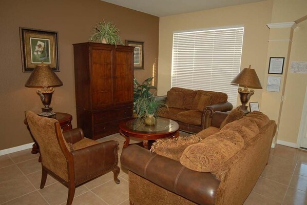 A living room with a brown leather sofa, two armchairs, a wooden cabinet, and a glass coffee table.