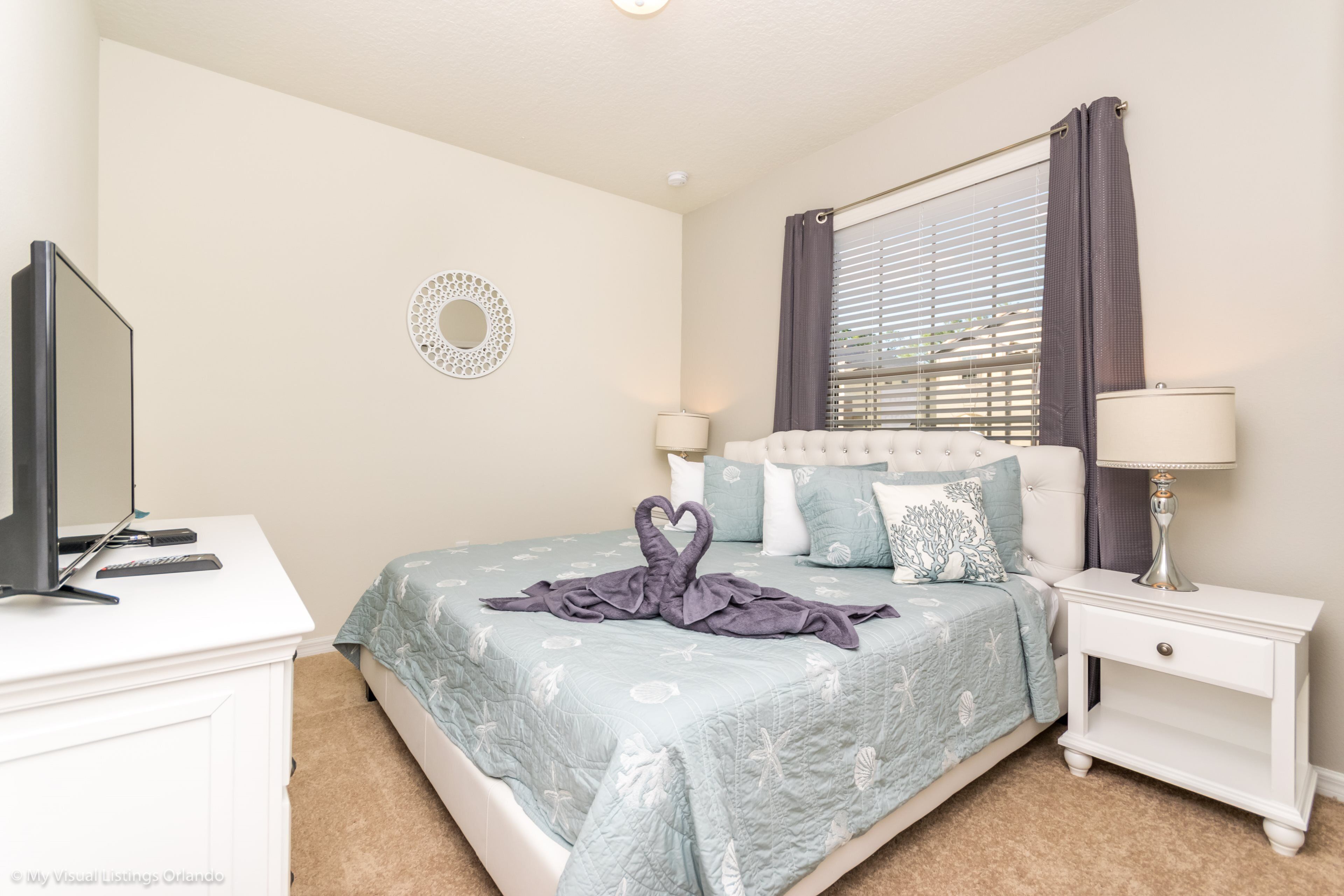 A bedroom with a bed, bedside tables, a TV, and a decorative wall piece.
