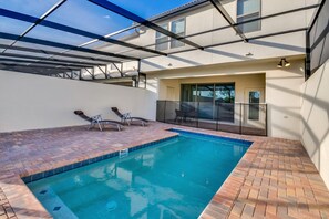 A swimming pool with a glass enclosure, a patio area with seating, and a view of a building. - 8810geneve (Kissimmee)