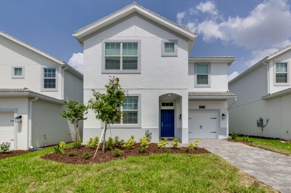 A two-story residential building with a blue front door, white exterior walls, and a small tree in the front yard. - 6 Bedroom Golf Course Resort Villa (Davenport)