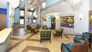 Een ruime lobby met een hoge plafond, houten balken en een centraal zithoek met kleurrijke stoelen.