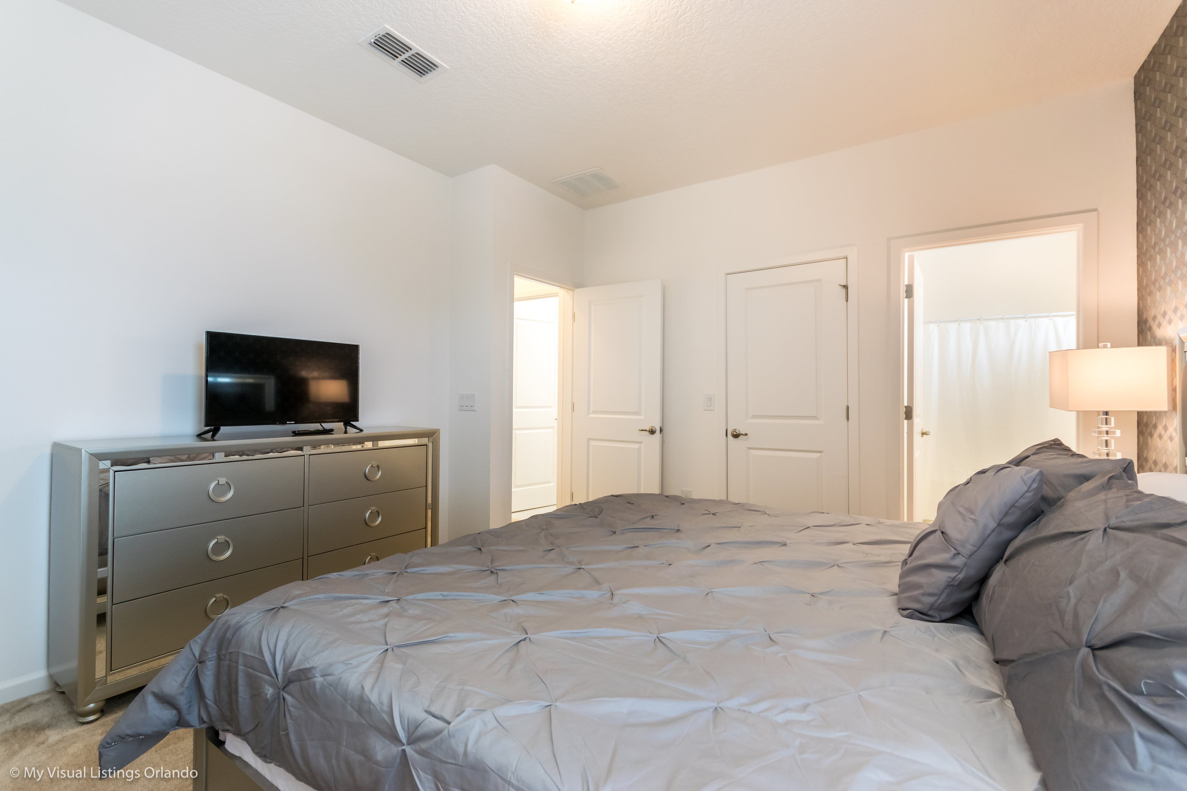 A bedroom with a bed, dresser, television, and two doors.