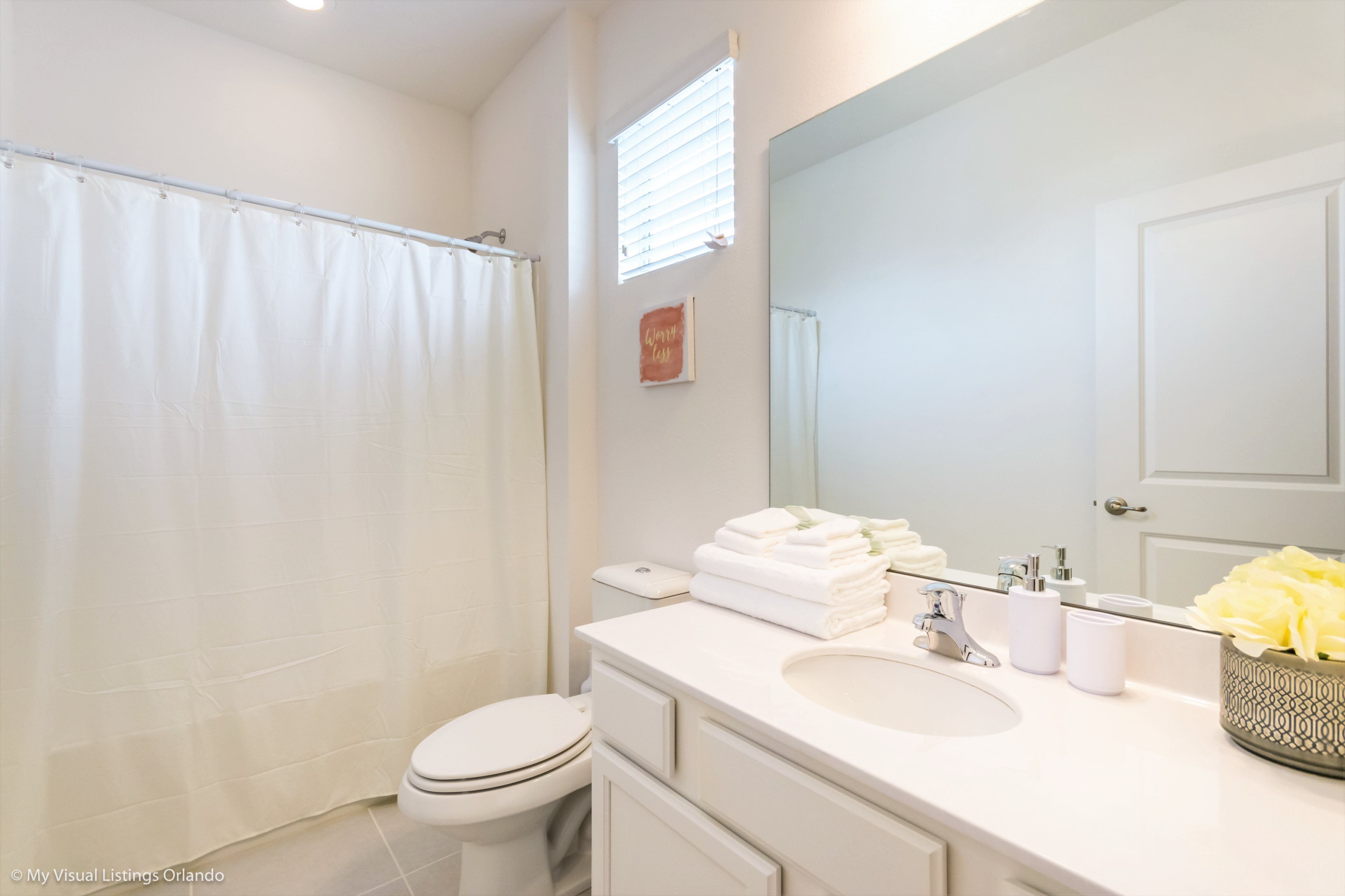 A bathroom with a toilet, a sink, a mirror, and a shower curtain.